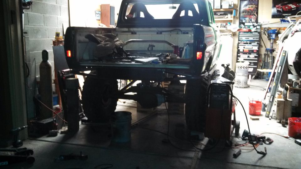 Rear view of a lifted pickup truck with large tires, undergoing modifications in a garage