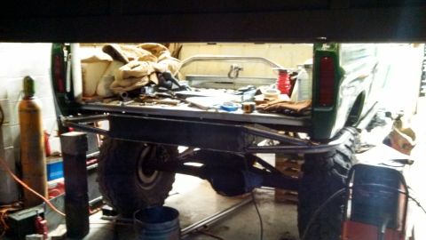 1967 Ford F-250 - The rear of a green pickup truck is shown, with its bed filled with various items and tools, and a custom bumper installed.