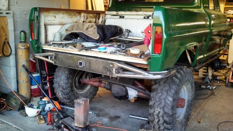 1967 Ford F-250 - A custom-built pickup truck with off-road tires and a roll cage is parked in a workshop.
