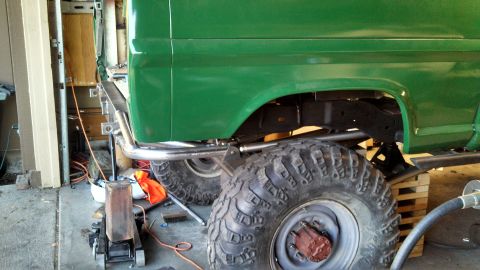 1967 Ford F-250 - Side view of a green pickup truck with large tires, undergoing maintenance in a garage setting.