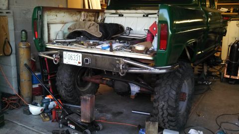 1967 Ford F-250 - Rear view of a 1967 Ford F-250 pickup truck, modified with a custom bumper and oversized tires, in a workshop setting.