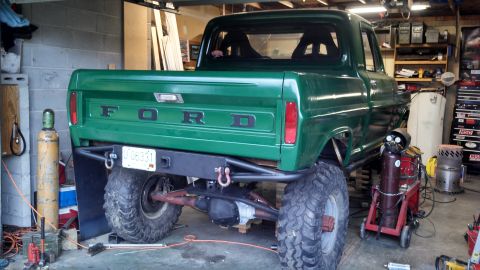 1967 Ford F-250 - A modified green pickup truck sits in a garage, showing off its lifted suspension and custom rear bumper.