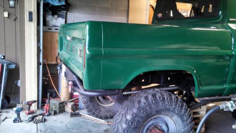 1967 Ford F-250 - The rear of a green 1967 Ford F-250 pickup truck is visible, modified with a lift kit and oversized tires.