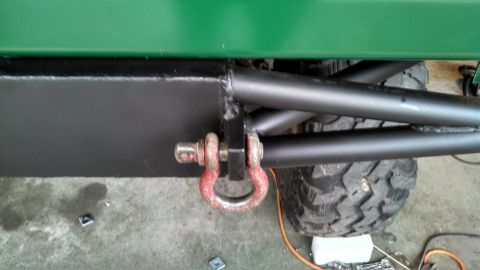 1967 Ford F-250 - Close-up view of a green truck's frame, showing a black box section with a red tow shackle and a large off-road tire.