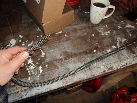 2004 Mercury Grand Marquis - A hand holds a flexible metal coil on a workbench next to a coffee mug and a cardboard box.