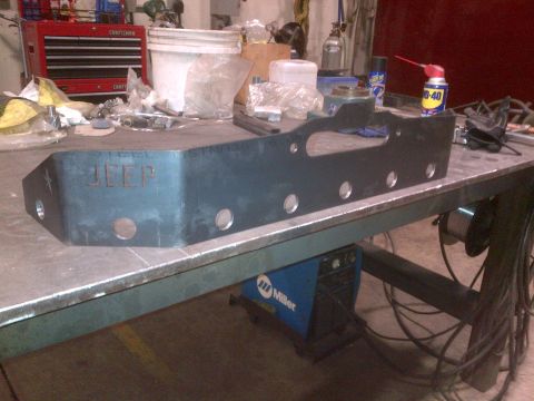 1985 Jeep CJ7 - A fabricated steel part with 'JEEP' stamped into it rests on a workbench next to tools and equipment.