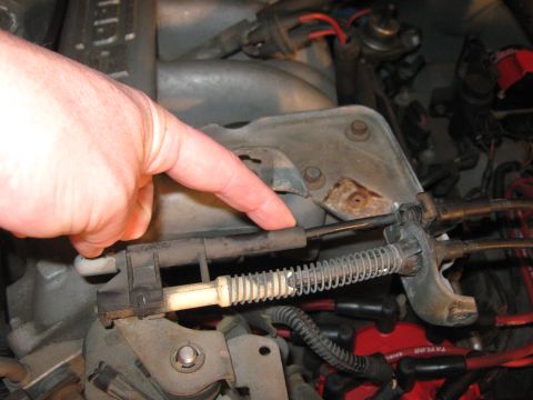 1996 Ford Bronco - Close-up of a hand indicating a cable mechanism within a vehicle's engine compartment.