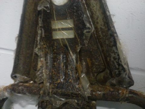 1994 Ford Bronco - Close-up of a heavily rusted metal bracket, partially covered in protective plastic wrap.