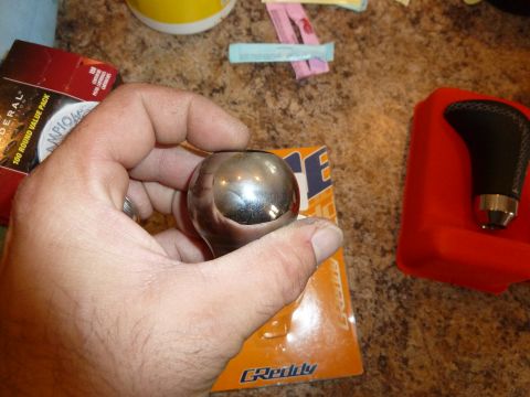 2007 Subaru Impreza - Chrome shift knob held in hand, next to another shift knob and packaging.