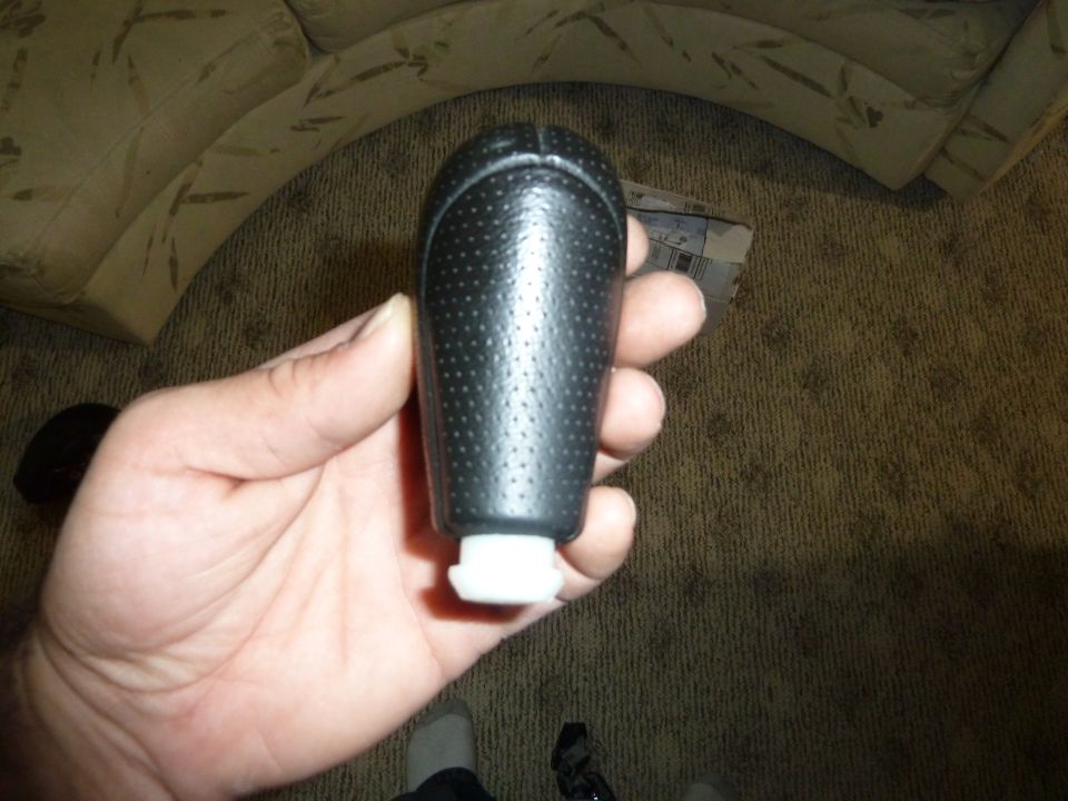 Hand holding a black perforated gear shift knob with a white plastic base