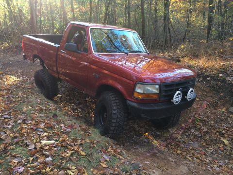1996 Ford F-150 - This red 1996 Ford F-150 is captured navigating a wooded trail with its off-road tires.