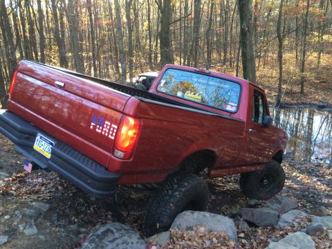 1996 Ford F-150 - 1996 Ford F-150 navigating rocky terrain in a forest setting.