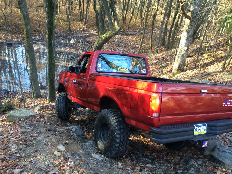 Red pickup truck with lifted suspension and off-road tires on a dirt path