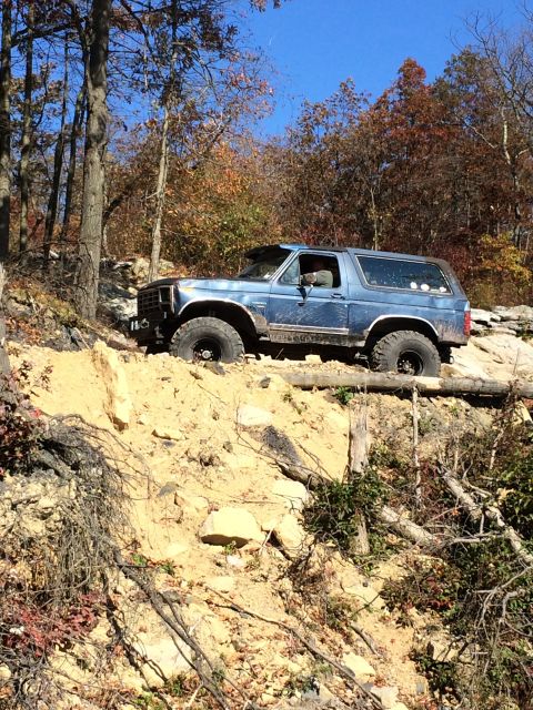 1996 Ford F-150 - A blue SUV navigates a challenging off-road trail with steep inclines and loose dirt.