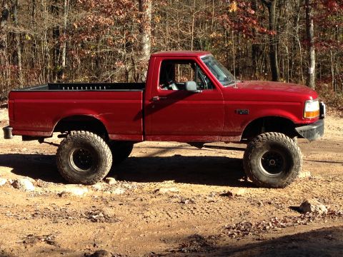 1996 Ford F-150 - This red 1996 Ford F-150 pickup truck is shown in profile, equipped with a lifted suspension and large off-road tires, ready for terrain.