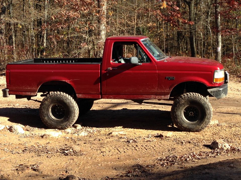 Side view of a red 1996 Ford F-150 pickup truck with lifted suspension and off-road tires