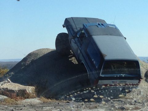1996 Ford F-150 - A blue SUV with oversized tires navigates a steep, rocky incline.