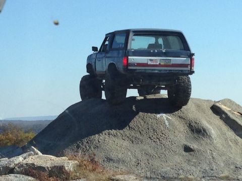 1996 Ford F-150 - Modified SUV with oversized tires navigates a steep, rocky terrain under a clear blue sky.