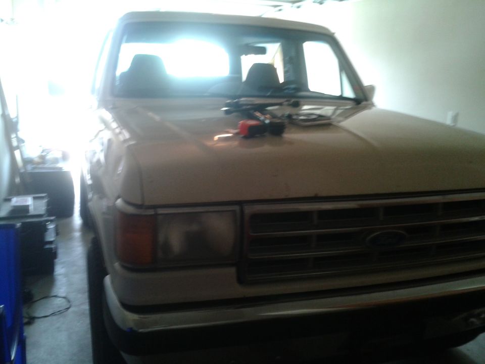 Front of a dusty tan Ford Bronco in a garage with tools on the hood
