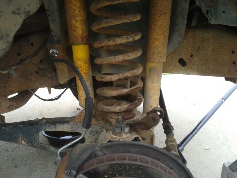 1988 Ford Bronco - Close-up view of the rear suspension system of a vehicle, showing worn components and brake assembly.