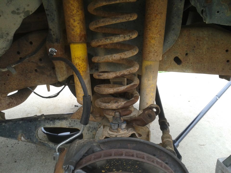 Rear suspension with rusty coil springs and yellow shock absorbers. Brake rotor and caliper visible below