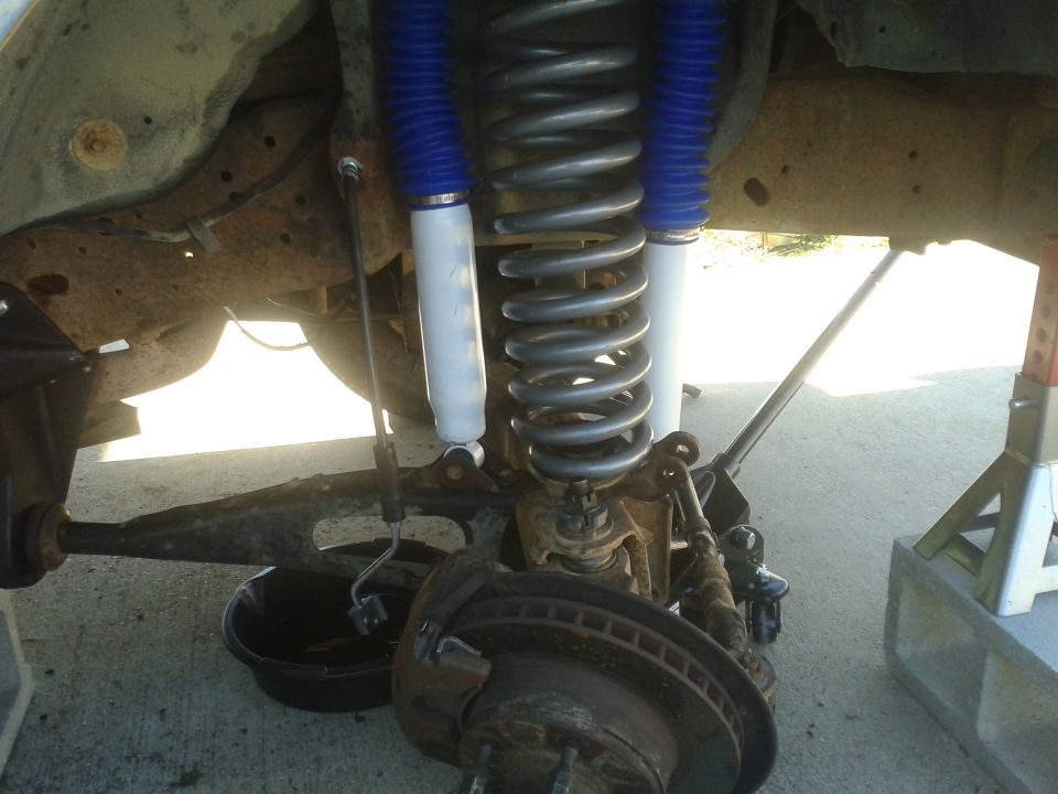Front suspension and brake assembly with coil spring and shock absorber. Oil drain pan visible