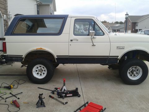 1988 Ford Bronco - 1988 Ford Bronco parked outside with various automotive tools and jacks around it.