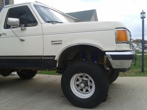 1988 Ford Bronco - This white Ford Bronco is shown from the front quarter panel, highlighting its lifted suspension and off-road tires.