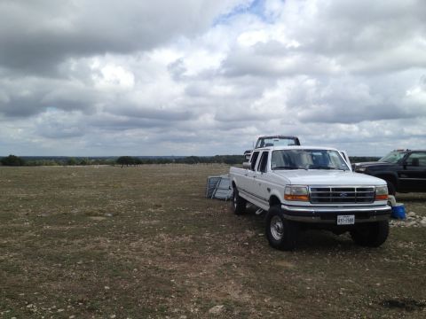 1997 Ford F-350 - A white 1997 Ford F-350 pickup truck is parked in a field with other vehicles and a wide expanse of sky.