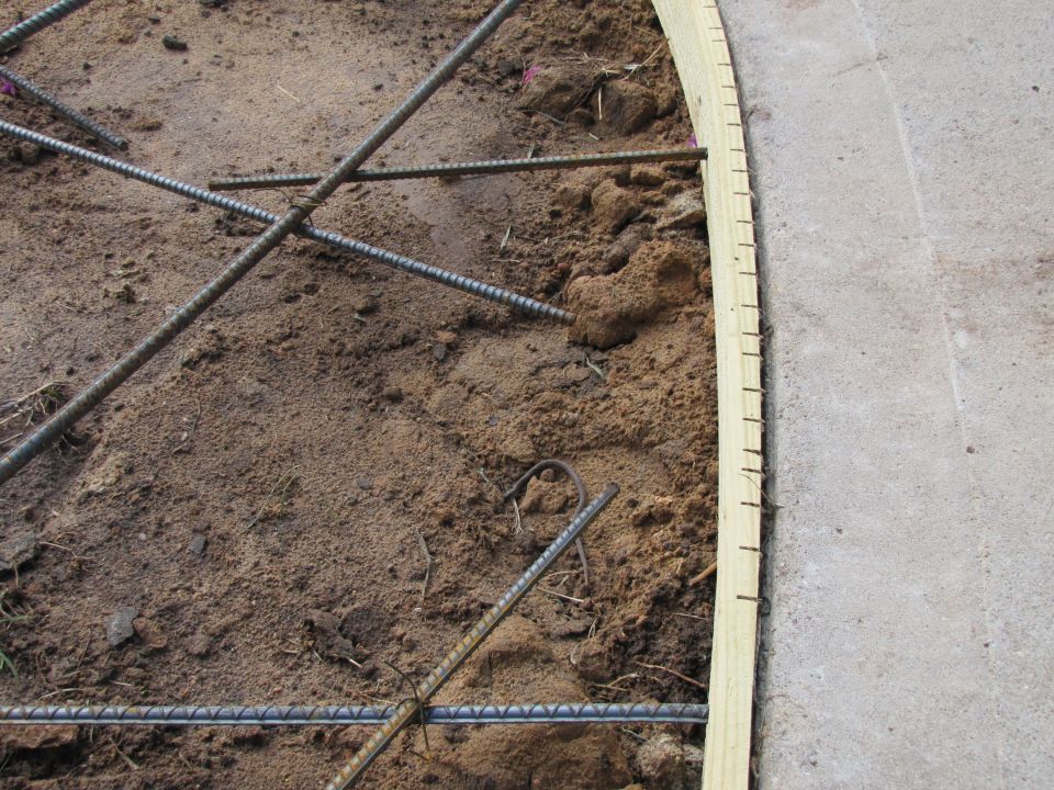 Construction rebar laid out on dirt with wooden formwork and concrete edge