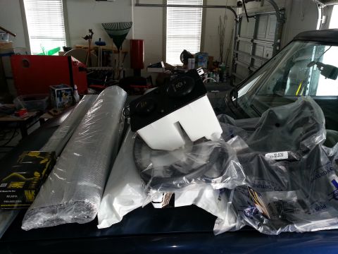 1994 Ford Bronco - Various parts and materials are piled on the hood of a dark-colored vehicle, obscuring the view of the car itself.