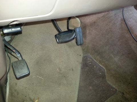 1994 Ford Bronco - Close-up view of the pedals and brake release lever inside a vehicle's cabin.