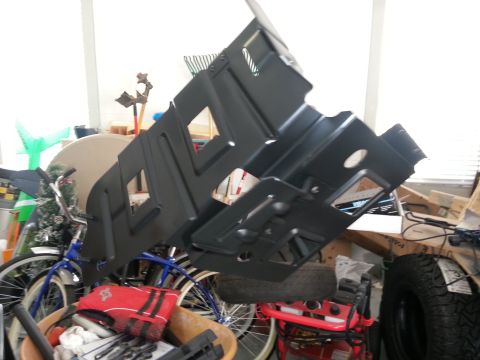 1994 Ford Bronco - A black metal undercarriage shield is displayed in a garage, surrounded by various items.