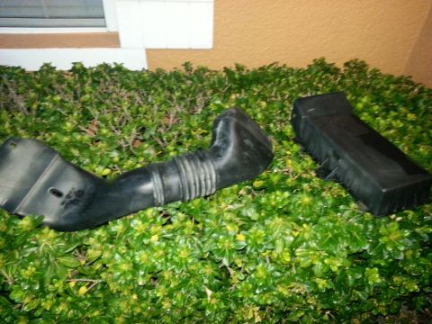 1994 Ford Bronco - Air intake components are shown resting on dense green foliage.