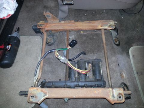 1994 Ford Bronco - A disassembled vehicle seat frame with exposed wiring and electrical modules sits on a carpeted surface.