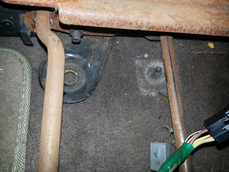 Close-up of rusty seat mounting hardware and wiring harness in a vehicle interior