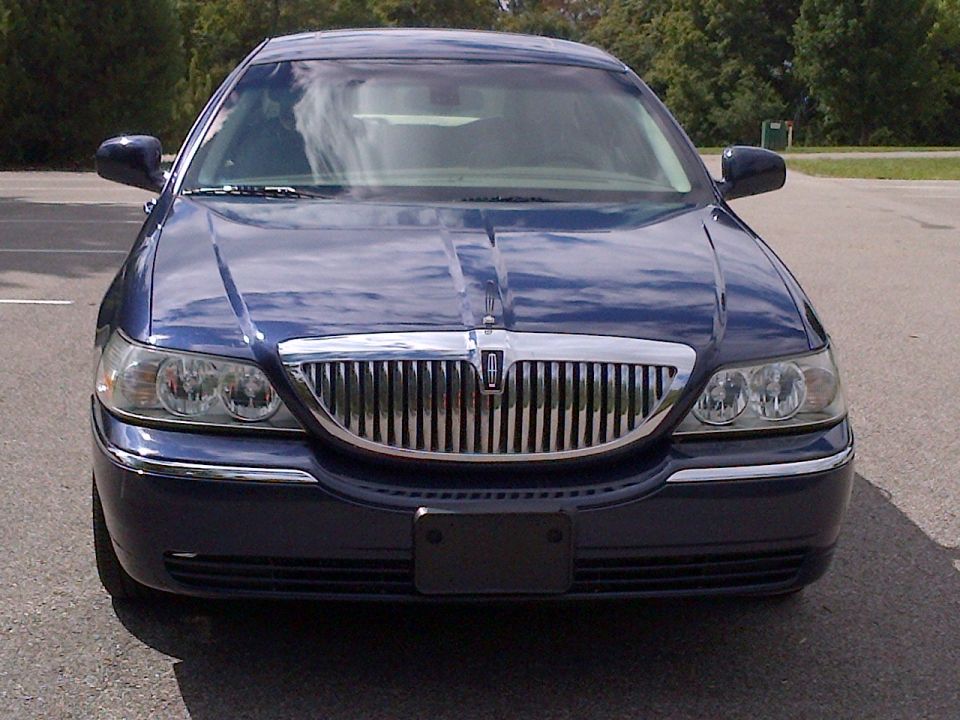 Dark blue Lincoln Town Car front view. Chrome grille with Lincoln emblem. Headlights visible