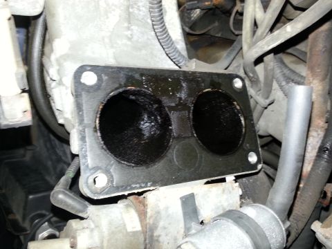 1994 Ford Bronco - A close-up view of a dirty throttle body gasket, showing significant carbon buildup within its passages.