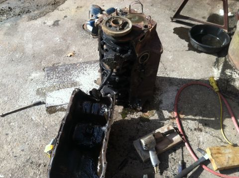 1978 Ford Bronco - Engine block and oil pan removed from a vehicle, resting on a concrete surface with tools nearby.