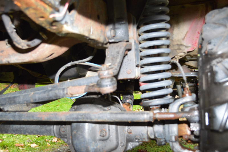 Close-up of vehicle's front suspension, showing coil spring, axle, and steering linkage
