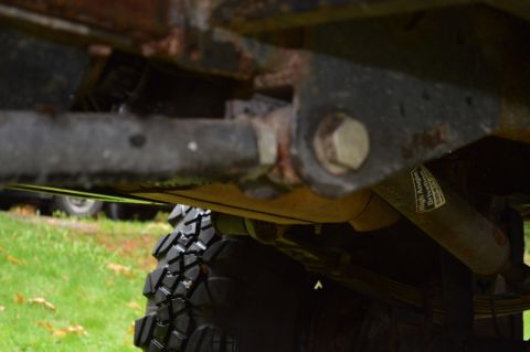 1989 Ford Bronco - Close-up of a vehicle's undercarriage, highlighting suspension components and a tire, with visible text on a shock absorber.