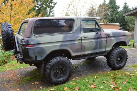 1989 Ford Bronco - Camouflaged Ford Bronco parked on a gravel driveway with fall foliage in the background.