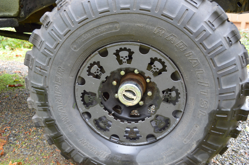 Close-up of a large off-road tire with "SUPER SWAMPER RADIAL LST" text and a custom black wheel with skull cutouts