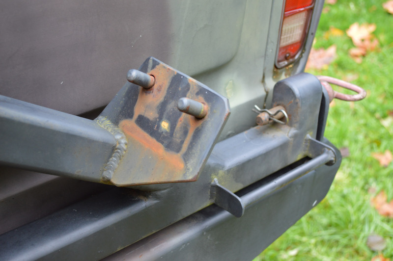 Close-up of a tow hitch mount attached to a vehicle's rear bumper. Shows rusty metal and pins