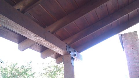 1996 Ford Bronco - The underside of a wooden porch roof shows beams, rafters, and planking, with a brick structure to the side.
