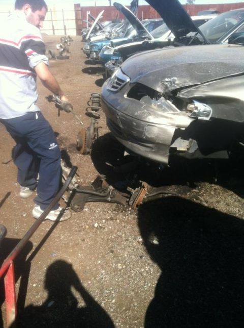1995 Ford Probe - A person works on a damaged car at a junkyard, with several other vehicles visible in the background.