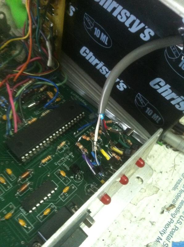 Close-up of an electronic circuit board with integrated circuits, resistors, and wiring. A gray cable connects to the board