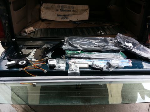 1994 Ford Bronco - Various car parts are laid out on the tailgate of a vehicle, with a box visible in the cargo area.