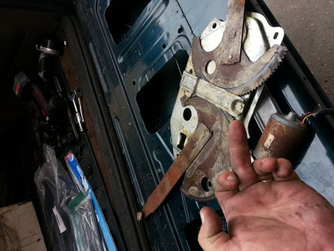 1994 Ford Bronco - hand gives a peace sign next to a rusty manual window regulator and motor pulled from a vehicle door panel.
