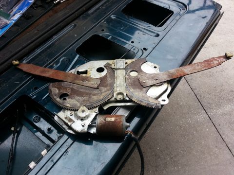 1994 Ford Bronco - A close-up view of a rusty window regulator mechanism with its motor attached.
